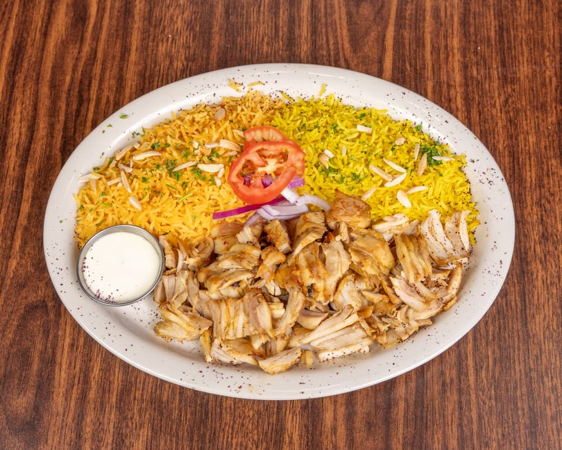 Chicken shawarma plate with yellow rice, sliced tomatoes, red onions, and a side of white sauce.