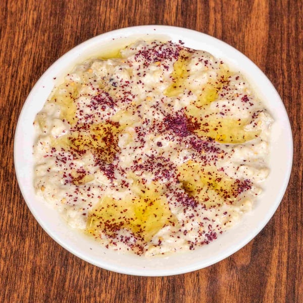 Creamy white dip with olive oil and red spice on a white plate, on a wooden table.