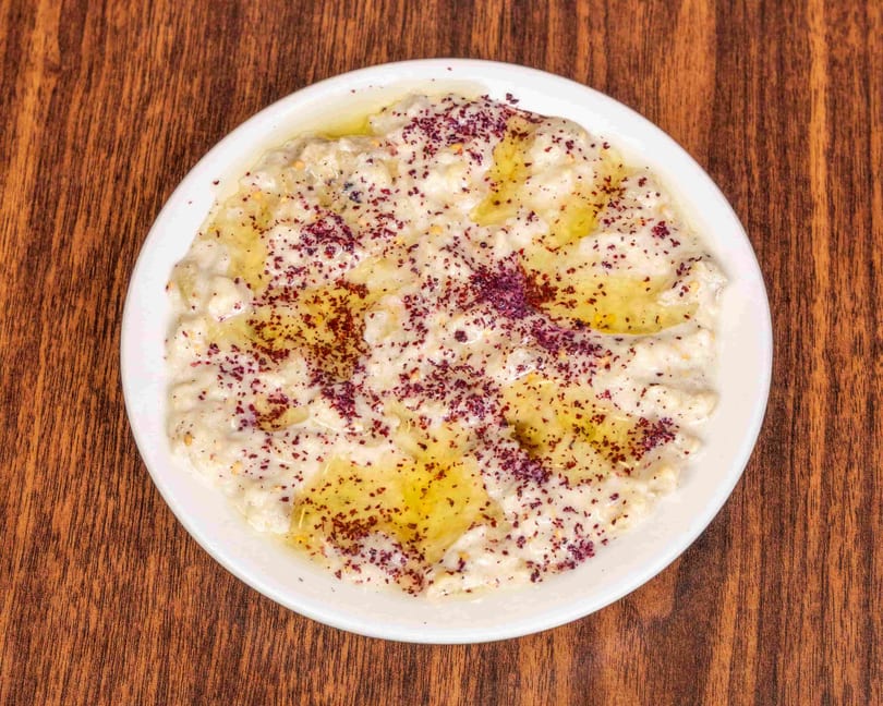 Creamy white dip with olive oil and red spice on a white plate, on a wooden table.