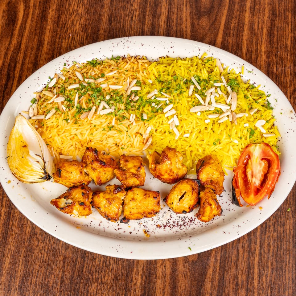 Chicken shish tawook with yellow rice, almonds, parsley, grilled onion, and tomato on a white plate.