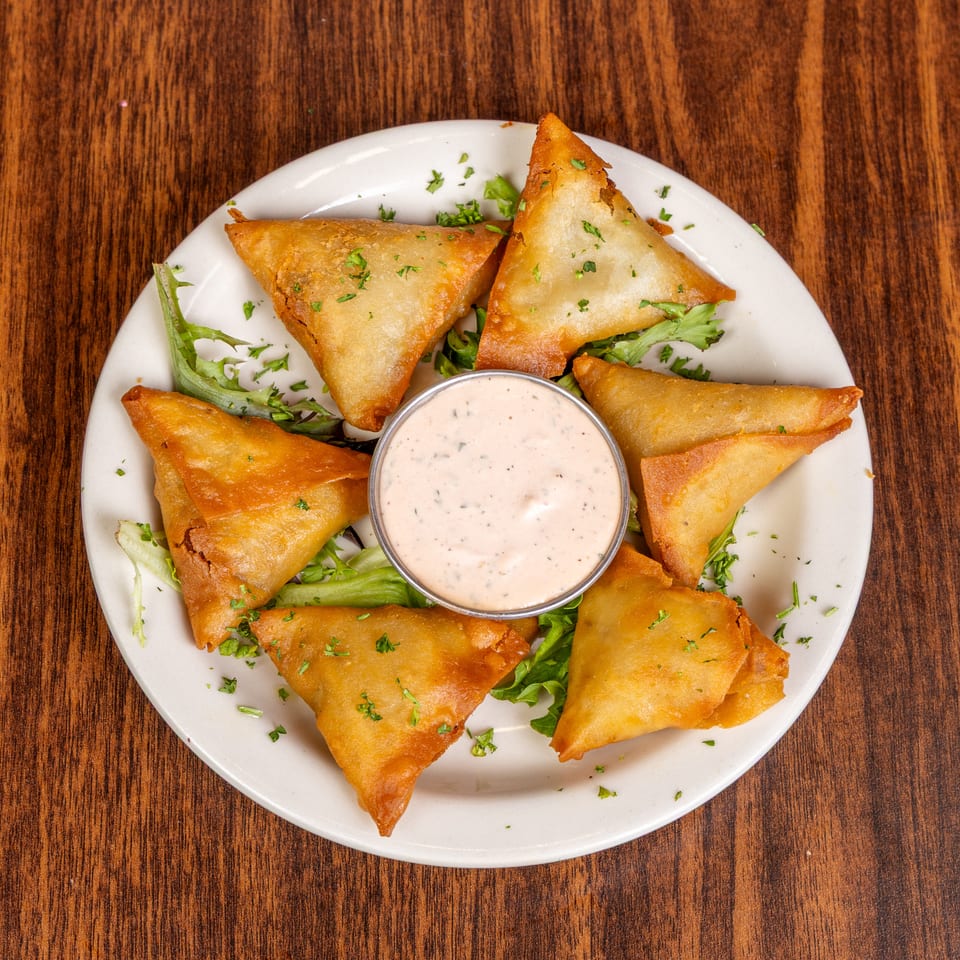 Golden-brown samosas arranged around a dipping sauce on a white plate with lettuce and parsley.