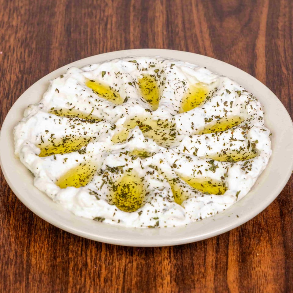 A white plate of labneh, drizzled with olive oil and sprinkled with dried mint, on a wooden table.