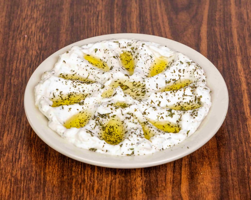A white plate of labneh, drizzled with olive oil and sprinkled with dried mint, on a wooden table.