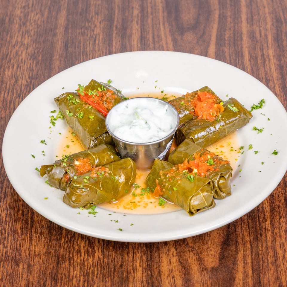 Grape leaves stuffed with rice and herbs, topped with tomato sauce and served with tzatziki.