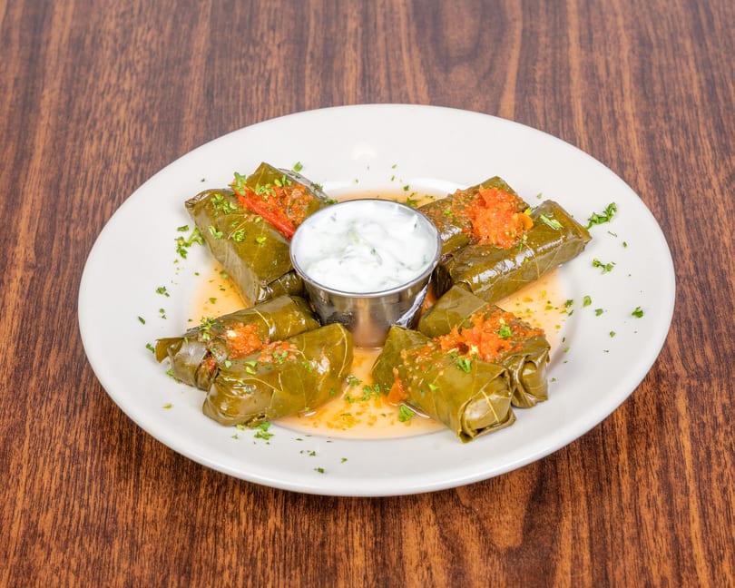 Grape leaves stuffed with rice and herbs, topped with tomato sauce and served with tzatziki.