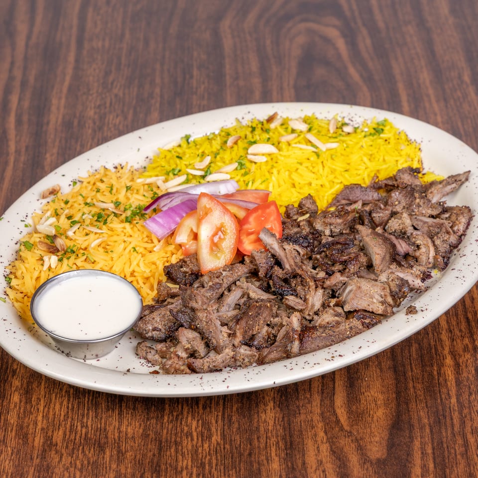 Shawarma plate with seasoned meat, yellow rice, sliced tomatoes, red onions, and a side of white sauce.