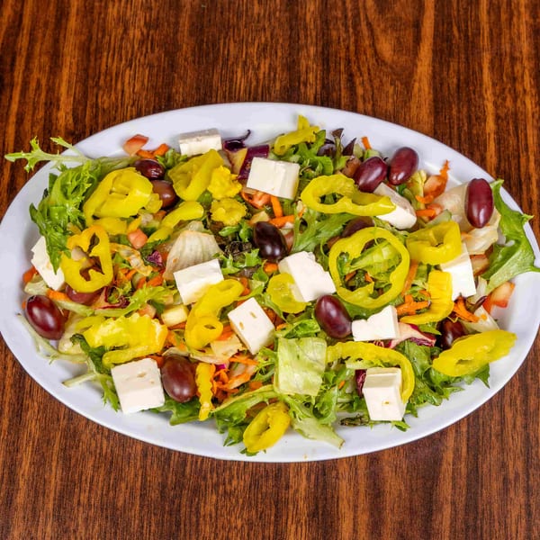 A vibrant salad with lettuce, pepperoncini, olives, and feta cheese on a white plate.