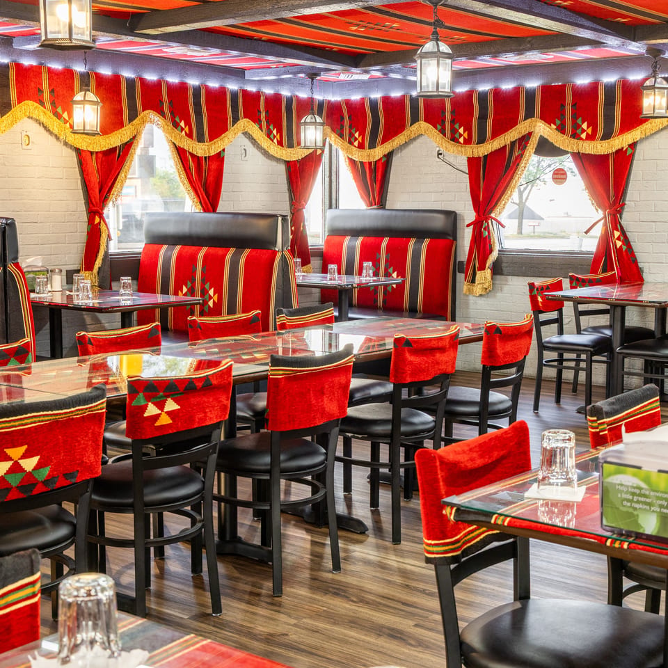 Restaurant interior with red and black patterned seating, red curtains, and glass-topped tables.
