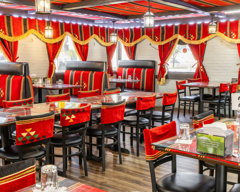 Restaurant interior with red and black patterned seating, red curtains, and glass-topped tables.