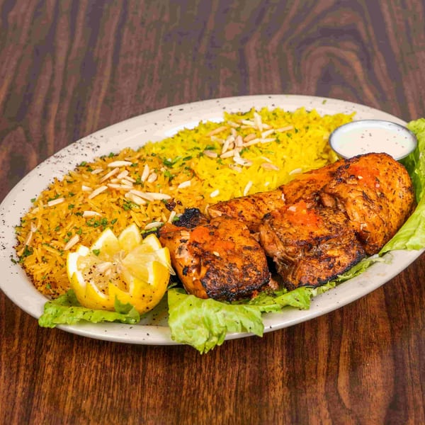 Grilled chicken with yellow rice, garnished with almonds, parsley, lemon, and a side of sauce.