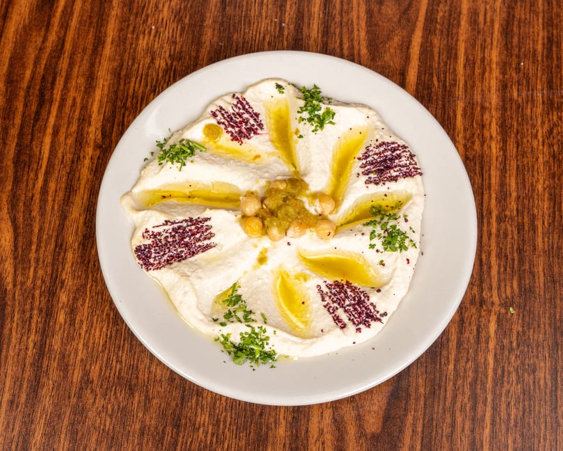 Creamy hummus drizzled with olive oil, garnished with chickpeas, green relish, sumac, and parsley.