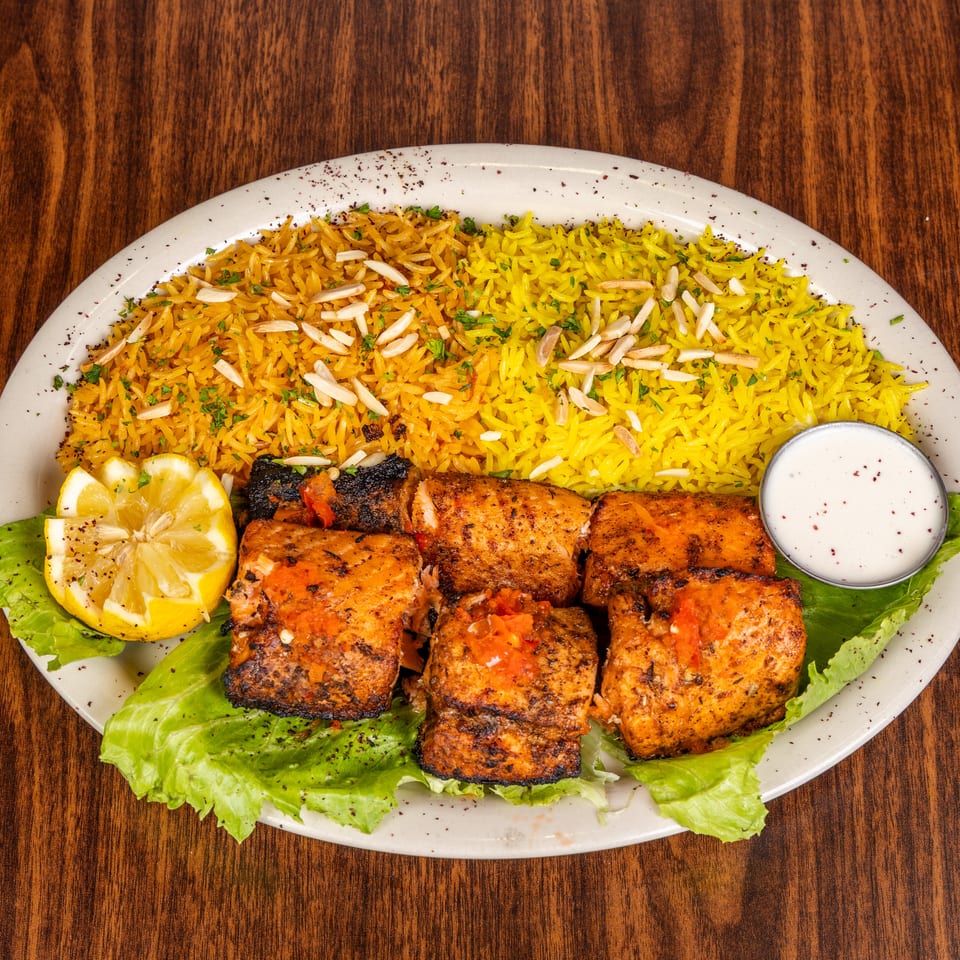 Grilled chicken skewers with yellow rice, lettuce, lemon, and a side of white sauce.