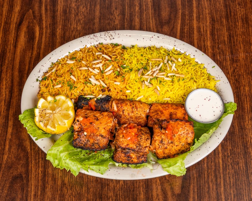 Grilled chicken skewers with yellow rice, lettuce, lemon, and a side of white sauce.