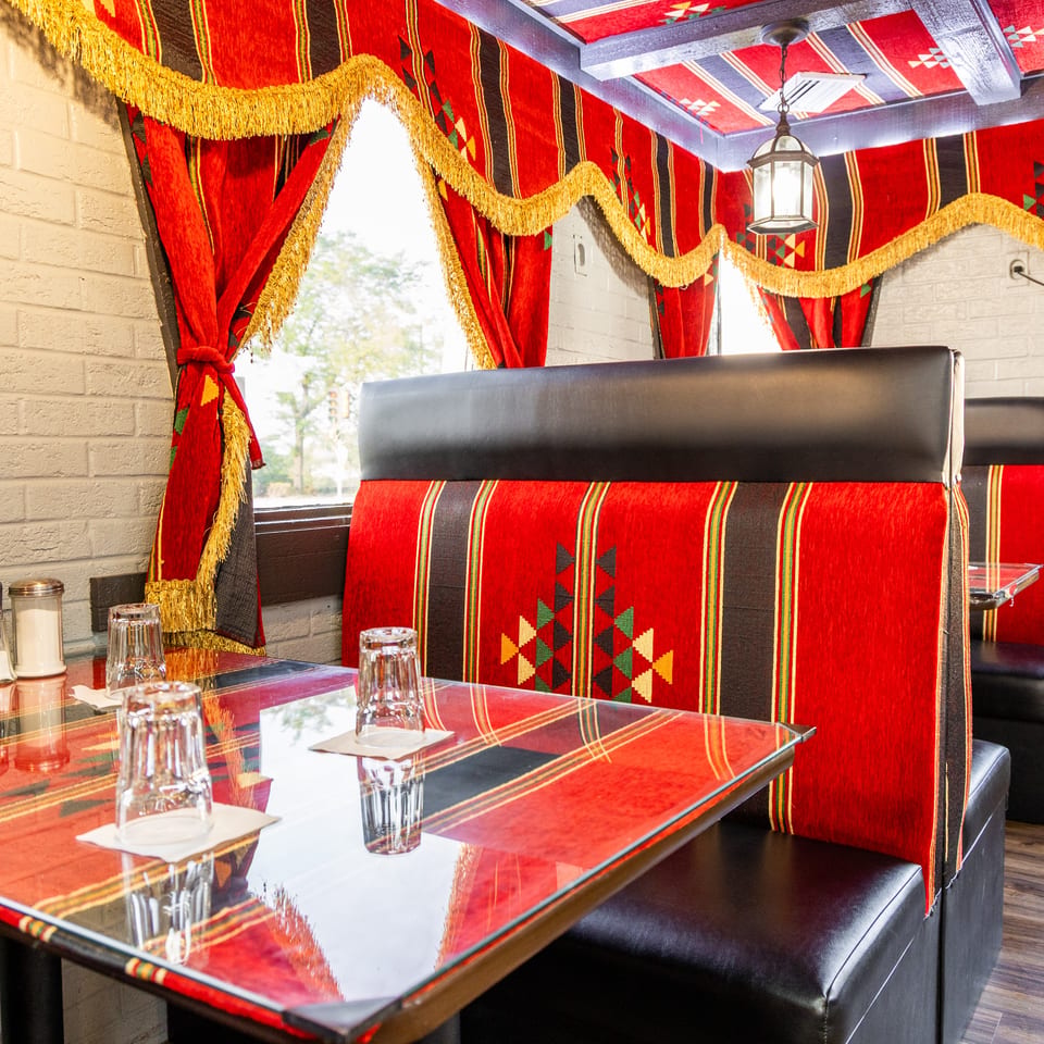 Restaurant interior with red and black patterned booths, glass-topped tables, and matching curtains with gold fringe.