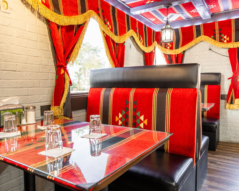Restaurant interior with red and black patterned booths, glass-topped tables, and matching curtains with gold fringe.
