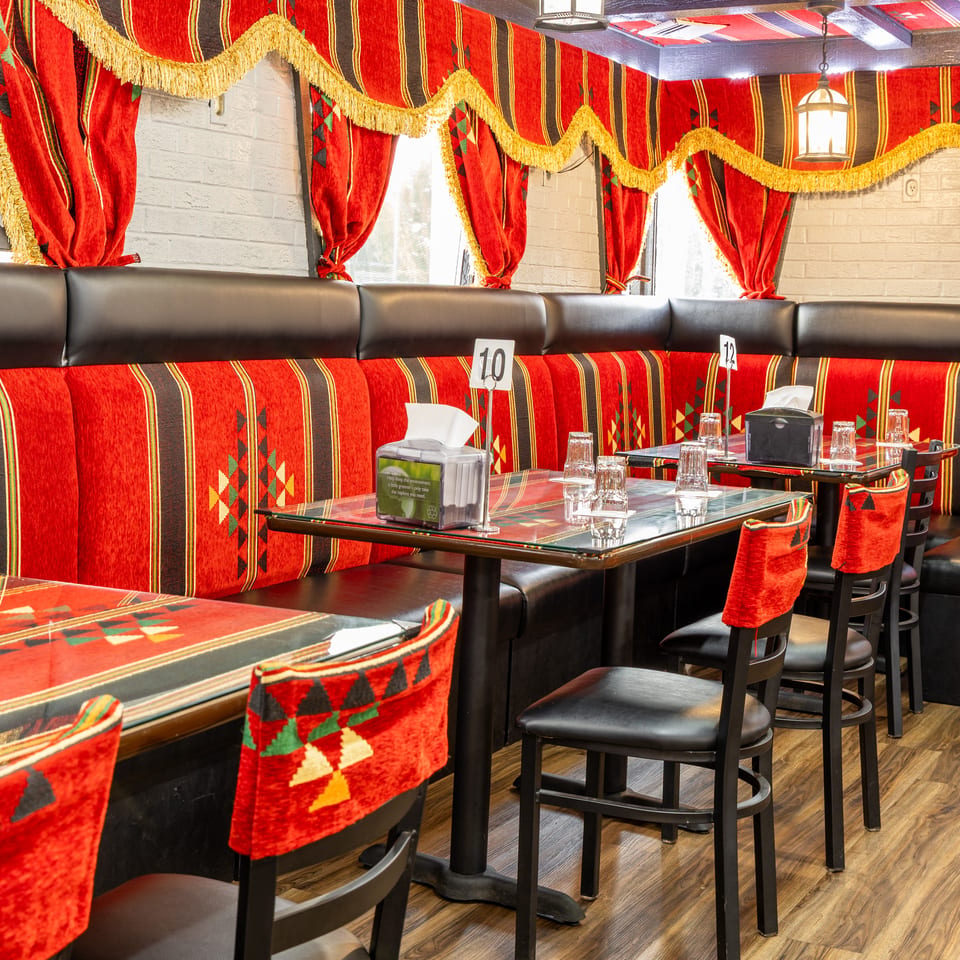 Restaurant interior with red and black patterned booths, glass-top tables, and black chairs with red fabric.