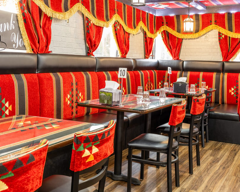 Restaurant interior with red and black patterned booths, glass-top tables, and black chairs with red fabric.