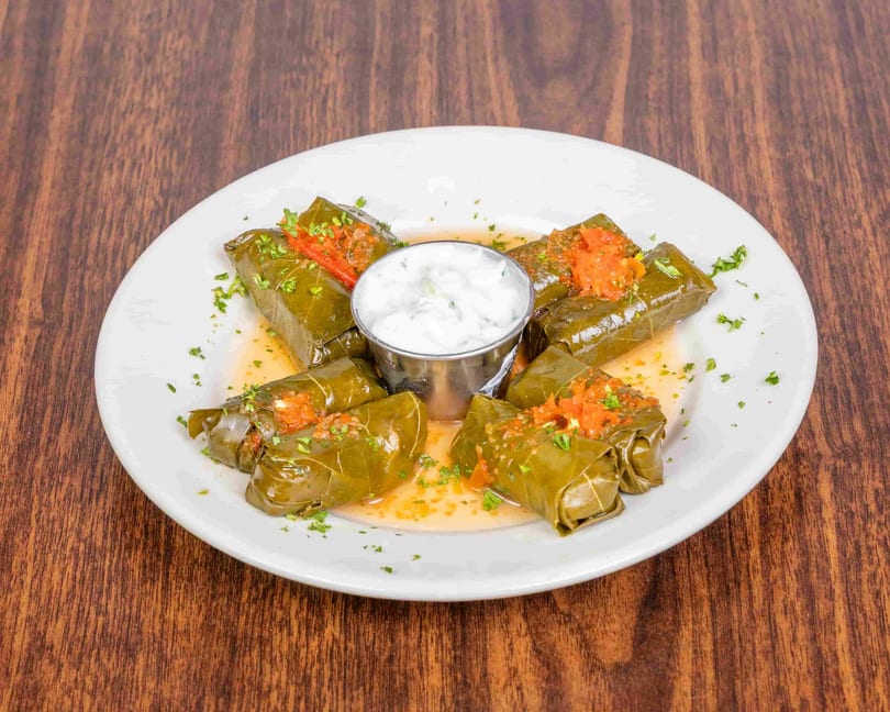 Grape leaves stuffed with rice and herbs, topped with red sauce and served with tzatziki.