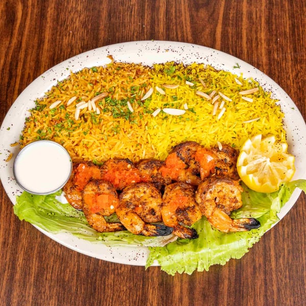 Grilled shrimp with tomato topping, yellow rice, lettuce, lemon, and a side of white sauce.
