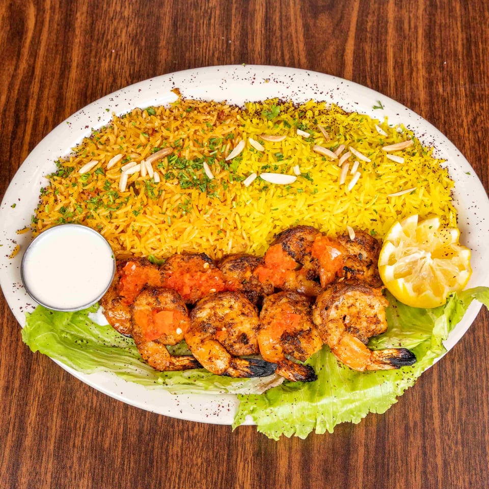 Grilled shrimp with tomato topping, yellow rice, lettuce, lemon, and a side of white sauce.