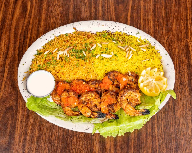 Grilled shrimp with tomato topping, yellow rice, lettuce, lemon, and a side of white sauce.