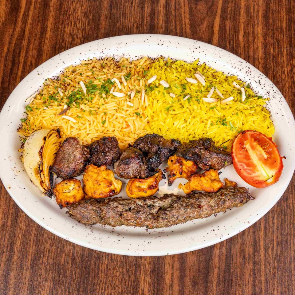 A white plate with yellow rice, various grilled meats, a grilled onion, and a tomato half.