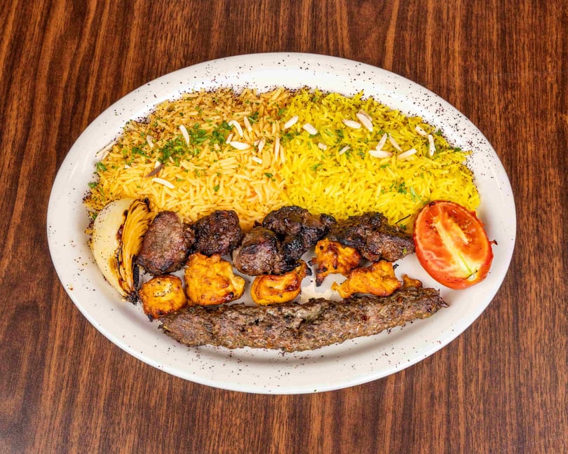 A white plate with yellow rice, various grilled meats, a grilled onion, and a tomato half.