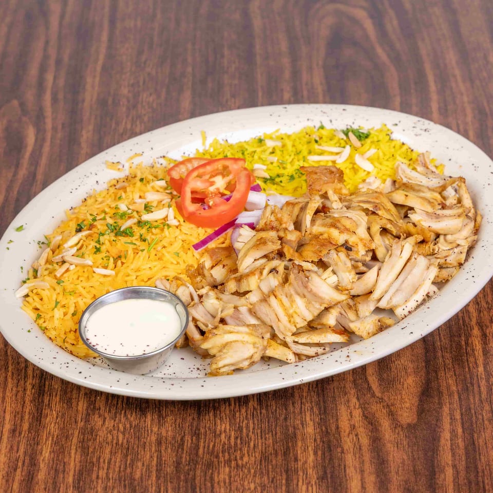 Chicken shawarma plate with yellow rice, sliced tomatoes, red onions, and a side of white sauce.