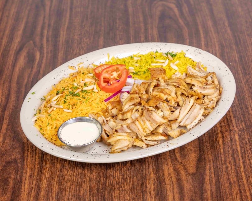 Chicken shawarma plate with yellow rice, sliced tomatoes, red onions, and a side of white sauce.