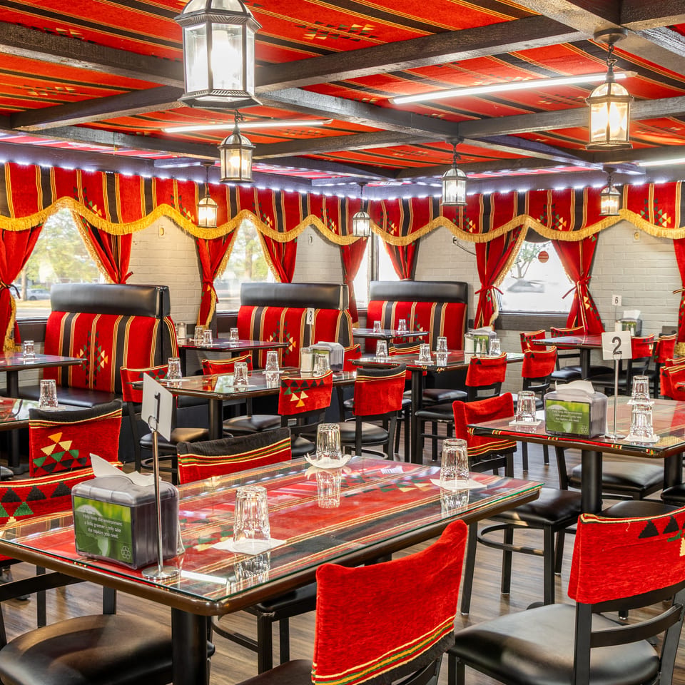 Restaurant interior with red and black patterned decor, set tables, and lanterns hanging from the ceiling.