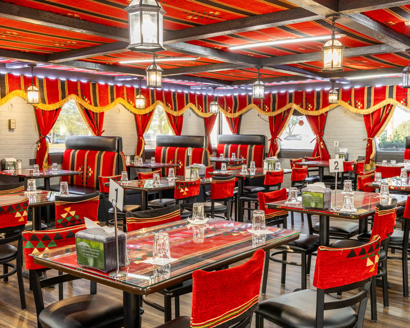 Restaurant interior with red and black patterned decor, set tables, and lanterns hanging from the ceiling.