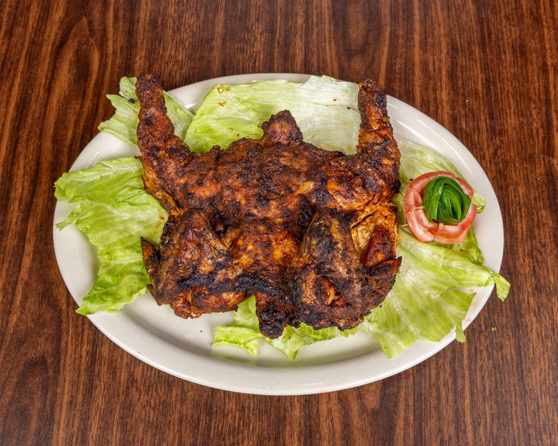 Grilled whole chicken, seasoned and charred, served on a bed of fresh lettuce with a tomato and cucumber garnish.