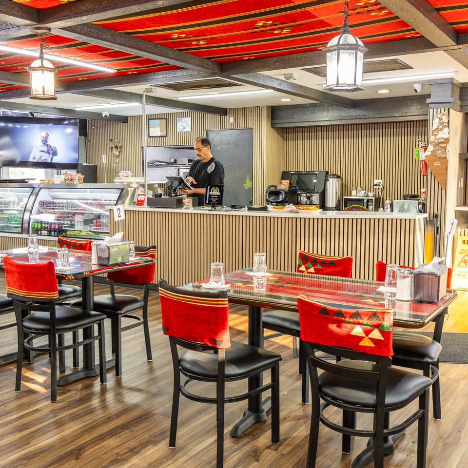 Restaurant interior with red and black patterned ceiling, empty tables, and a man working behind the counter.