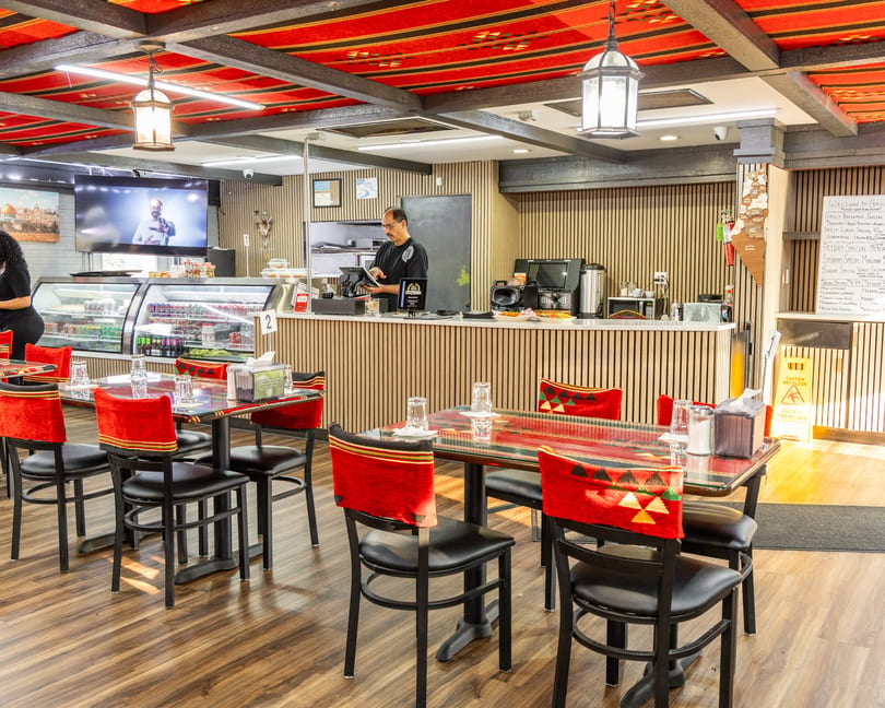 Restaurant interior with red and black patterned ceiling, empty tables, and a man working behind the counter.