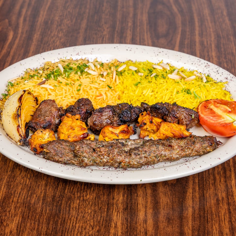 A platter of yellow rice, grilled meats, charred onion, and a tomato half on a wooden table.