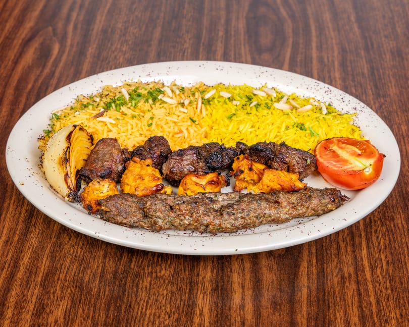 A platter of yellow rice, grilled meats, charred onion, and a tomato half on a wooden table.