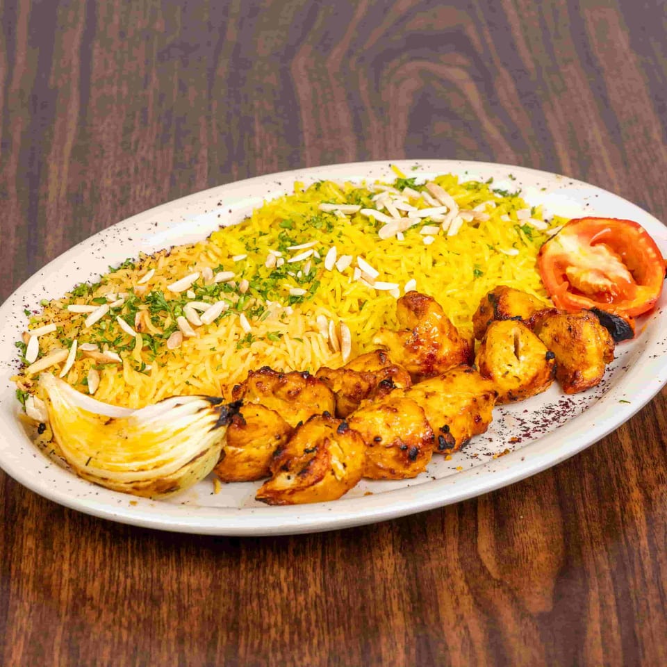 Chicken shish tawook with yellow rice, grilled onion, and tomato on a white plate.