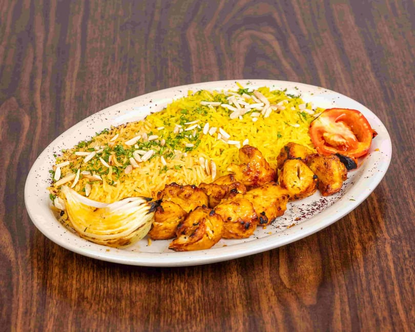 Chicken shish tawook with yellow rice, grilled onion, and tomato on a white plate.