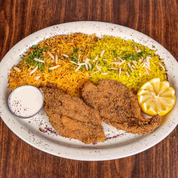 Fried fish fillets with yellow rice, almonds, parsley, a lemon wedge, and white sauce on a plate.