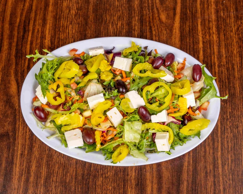 A vibrant salad with lettuce, pepperoncini, olives, and feta cheese on a white plate.