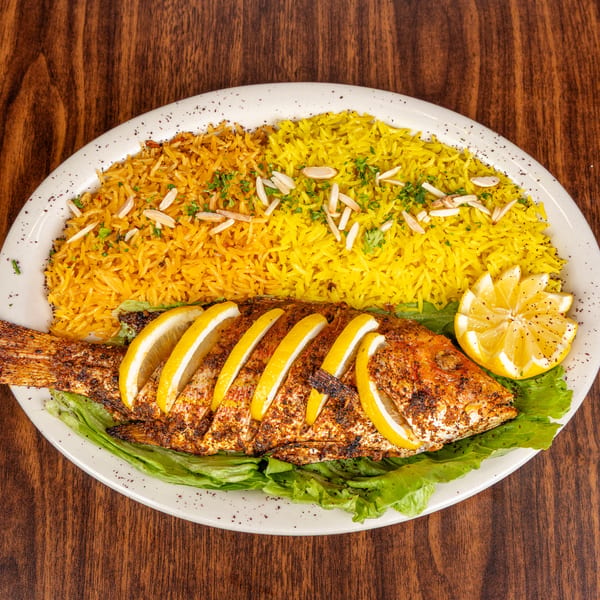 Whole grilled fish with lemon slices, served with yellow rice and lettuce on a white plate.